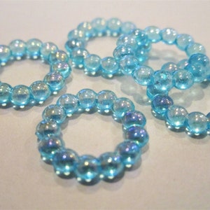 May include: Five iridescent blue rings made of small beads. The rings are all the same size and are arranged in a circle.