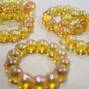 May include: Four iridescent yellow beaded rings. The beads are round and have a slight shimmer to them.