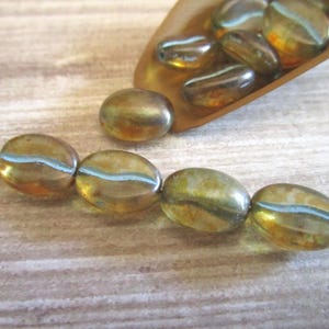 May include: A collection of oval-shaped glass beads with a translucent amber and brown mottled finish, featuring a distinct horizontal light blue stripe running through the center of each bead, with four beads strung on a thin metal wire.