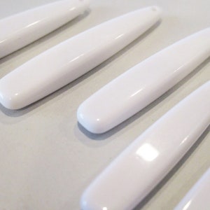 May include: Five white, smooth, oval-shaped ceramic beads. The beads are arranged in a row, with the ends of each bead slightly overlapping the next.