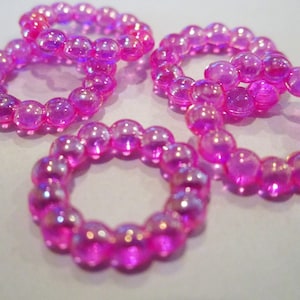 May include: Five iridescent pink beaded rings, each made of small, round beads. The rings are stacked on top of each other, creating a colorful and eye-catching display.