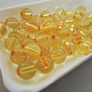 May include: A close-up of a white dish filled with translucent amber-colored beads. The beads are round and have a slight shine.