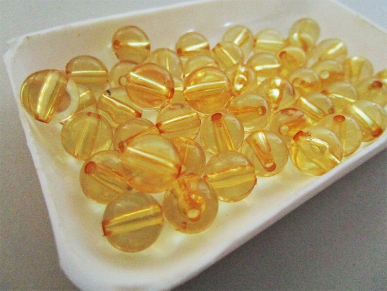 May include: A close-up of a white dish filled with translucent amber-colored beads. The beads are round and have a slight shine.