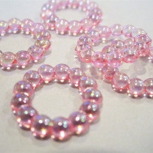 May include: Five iridescent pink beaded rings. The beads are translucent and have a slight shimmer.