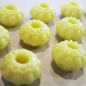 May include: A group of 10 yellow plastic beads with a raised, textured design. The beads have a hole in the center and are arranged in a semi-circle on a white surface.