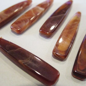 May include: Six brown and white marbled plastic hair clips. The clips are long and narrow, with a slightly rounded end.