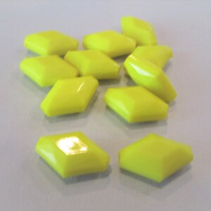 May include: A collection of eleven bright yellow, diamond-shaped objects. Each object has a slightly rounded top and bottom, with angled sides. The objects are scattered on a light gray surface, with some overlapping.