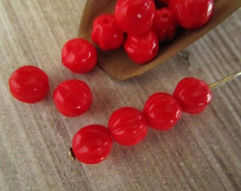 May include: Bright red, round beads with a marbled appearance. Some beads are loose, while others are strung on a gold-colored wire. A small brown scoop holds additional beads. The beads are a vibrant, glossy red.