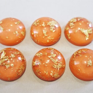 May include: Six round, orange cabochons with gold flecks. The cabochons are smooth and shiny.