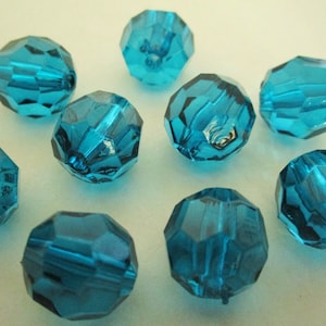 May include: A collection of ten faceted, teal-colored beads. Each bead has a multi-sided, geometric shape with a hole running through the center. The beads are made of a translucent material, reflecting light and creating a sparkling effect. Ideal for jewelry making.