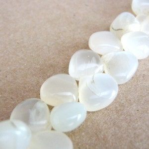 May include: A strand of white, smooth, oval-shaped beads. The beads are arranged in a line and are all the same size.