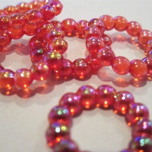 May include: Four iridescent pink beaded rings, each made of small, round beads. The rings are stacked on top of each other, creating a layered effect.