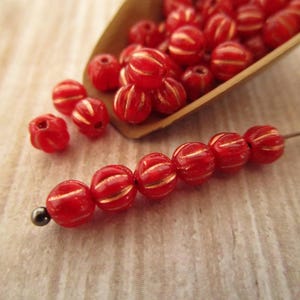 May include: Red glass beads with gold accents. The beads are round and have a textured surface. The beads are strung on a wire.