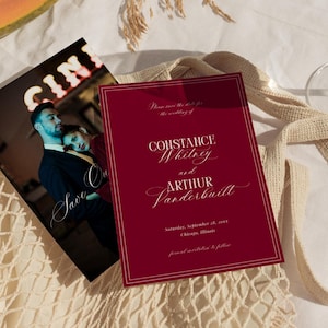 Könnte beinhalten: Eine bordeauxfarbene Hochzeitseinladung mit weißer Kalligraphie, mit den Namen Constance Whitney und Arthur Vanderbilt. Eine Foto-Save-the-Date-Karte ist sichtbar, zusammen mit einem Glas und einer beigen Tragetasche. Die Einladung enthält Datum und Ort der Hochzeit.