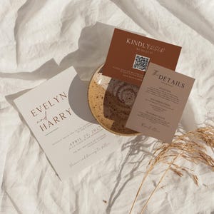 Puede incluir: Un juego de invitaciones de boda que incluye una tarjeta principal color crema con el texto Evelyn and Harry, una tarjeta RSVP marrón oscuro con un código QR y una tarjeta de detalles marrón claro, dispuestas alrededor de un cuenco de cerámica.