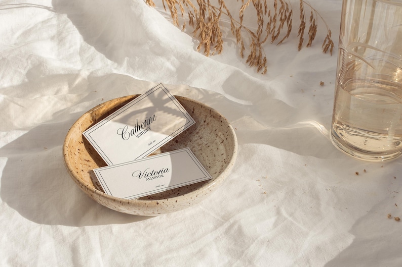 May include: Two white business cards with black text in a small, speckled, beige bowl. The top card reads "Catherine Whittier" and the bottom card reads "Victoria Alexander".