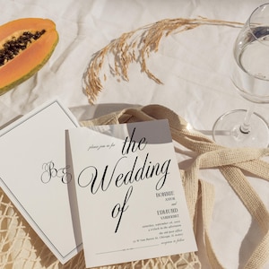 May include: A wedding invitation with a white background and black text. The invitation reads "The Wedding of Bonnie Astor and Edmund Vandererli" and includes the date and time of the wedding. The invitation is lying on a white surface with a brown woven bag and a papaya.