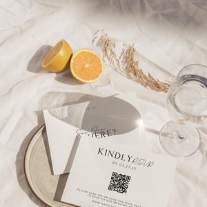 May include: A white card with black text that reads "See you there?" and "Kindly RSVP by 03.23.25". A QR code is included with the text "Please scan the QR code for more details and to RSVP via our wedding website www.weddingwebsite.com".