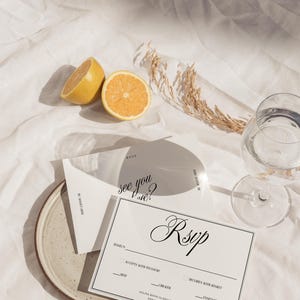 May include: A white RSVP card with black text that says "see you there?" and "RSVP". The card has a section for the guest's name, a checkbox for accepting or declining the invitation, and a choice of meal options: beef, chicken, or vegetarian.