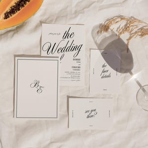 May include: Wedding invitation suite with white cards and black calligraphy. The cards include the text "the wedding", "B&E", "the finer details", and "see you there?"