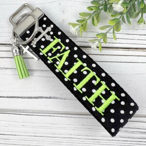 Pu&ograve; includere: Portachiavi in tessuto a pois neri e bianchi con un anello portachiavi argentato e un pon pon verde. Il portachiavi &egrave; ricamato con la parola "FAITH" in verde.