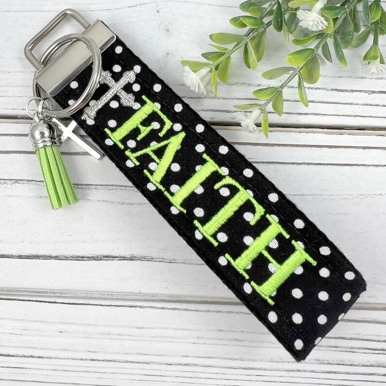 Pu&ograve; includere: Portachiavi in tessuto a pois neri e bianchi con un anello portachiavi argentato e un pon pon verde. Il portachiavi &egrave; ricamato con la parola "FAITH" in verde.