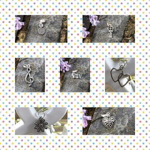 May include: A collection of silver charm pendants, including a treble clef, a key, a flower, two hearts, and a heart with a fleur-de-lis design. The charms are displayed on a variety of surfaces, including stone and wood.