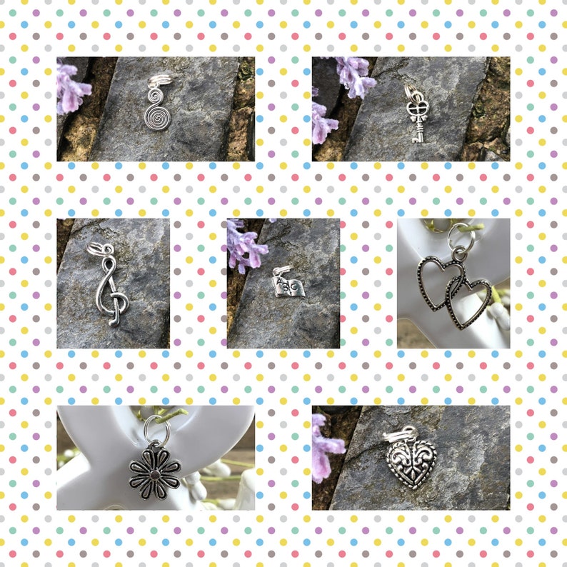 May include: A collection of silver charm pendants, including a treble clef, a key, a flower, two hearts, and a heart with a fleur-de-lis design. The charms are displayed on a variety of surfaces, including stone and wood.