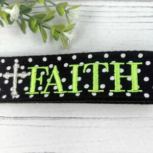 Pu&ograve; includere: Tessuto nero con pois bianchi e la parola "FAITH" ricamata in verde con una croce argentata a sinistra.