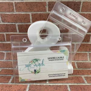 May include: A clear plastic badge holder with a business card inside. The card has a floral design and the text "sew much detail" and "Sandee Caudle Designer & Seamstress". The card also includes the website address "sewmuc@comporium.net" and "www.sewmucdetail.com".