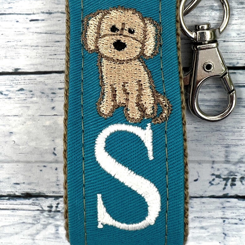 May include: Teal blue fabric key chain with a brown embroidered dog and a white embroidered letter S.