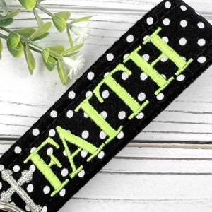 Pu&ograve; includere: Portachiavi in tessuto nero a pois bianchi con la parola "FAITH" ricamata in verde.