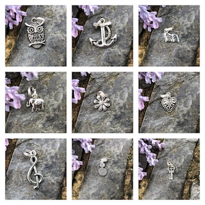 May include: Nine silver charm pendants on a gray background. The charms include an owl, anchor, alphabet flag, elephant, flower, heart, treble clef, spiral, and key.