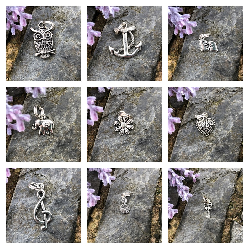 May include: Nine silver charm pendants on a gray background. The charms include an owl, anchor, alphabet flag, elephant, flower, heart, treble clef, spiral, and key.