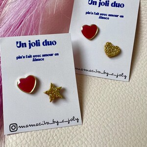 Peut inclure: Deux ensembles de broches avec le texte "Un joli duo" et "pin's fait avec amour en Alsace". Un ensemble comprend un cœur rouge et une étoile dorée. L'autre ensemble comprend un cœur rouge et un cœur doré.