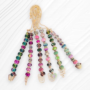 May include: A handcrafted, beaded octopus-shaped ornament. The ornament features a gold-colored head and tentacles adorned with colorful beads in shades of pink, green, blue, and purple. The tentacles have wire accents and are arranged on a white background.