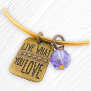 May include: A gold bangle bracelet with a charm that says "Live What You Love" and a purple crystal bead.