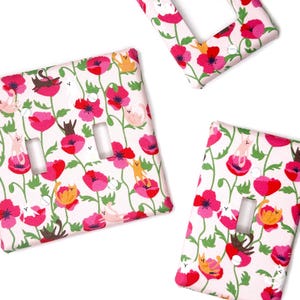 May include: Three fabric light switch covers with a floral and cat design. The covers feature a white background with red poppies and various colored cats. One cover has a single switch opening, one has two, and one has a rectangular opening.