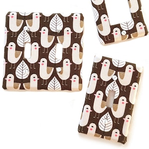 May include: A set of fabric light switch covers with a repeating pattern of white birds, brown leaves, and brown background. The covers are in various shapes for different switch configurations.