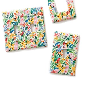 May include: Three light switch covers with a floral pattern. The covers are white with a colorful floral design featuring pink, yellow, blue, and green flowers. The switch covers are designed to fit a standard light switch.