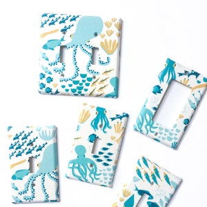 May include: Five light switch covers with a nautical theme. The covers feature an octopus, fish, and seahorse design in shades of blue, yellow, and white.