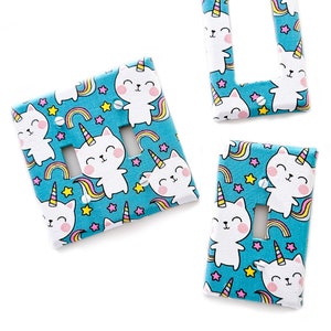 May include: Three light switch covers with a blue background and a pattern of white cats with unicorn horns, rainbows, and stars.
