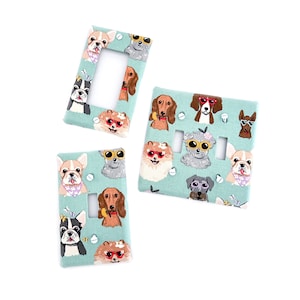 Puede incluir: Tres tapas de interruptor de luz con fondo azul claro y un patrón de perros con gafas de sol. Los perros son un Bulldog Francés, un Dachshund, un Pomerania, un Shih Tzu y un Beagle.