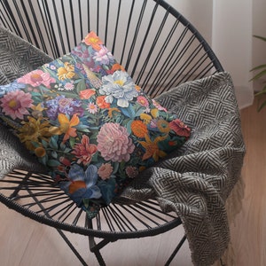 May include: A black metal chair with a gray and white patterned throw blanket and a floral patterned pillow. The pillow features a variety of flowers in shades of pink, blue, yellow, and green.