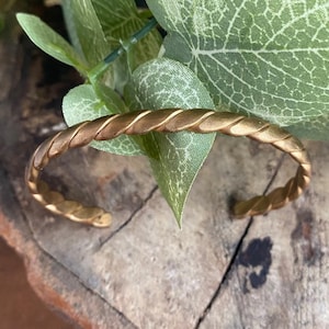Op de afbeelding: Een gouden, gedraaide draad armband. De armband is gemaakt van metaal en heeft een eenvoudig, elegant ontwerp.