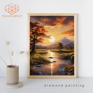 May include: Diamond painting of a sunset over a river with a mountain in the background. The river is flowing through a green meadow with trees on either side. The sky is a vibrant orange and pink with clouds. There are birds flying in the sky.