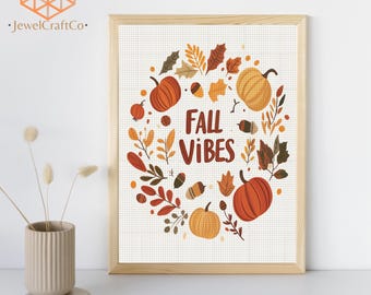 May include: A framed diamond painting featuring a wreath of orange and brown pumpkins, acorns, and autumn leaves surrounding the text FALL VIBES in dark red letters. The design is set against a white grid background within a light wood frame.