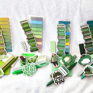 Peut inclure: Quatre ensembles de fournitures de papeterie sur le th&egrave;me du vert, comprenant des autocollants de piles de livres, des blocs de notes adh&eacute;sives dans diverses nuances de vert, des stylos verts et des autocollants avec des phrases comme "Run Forest Run".