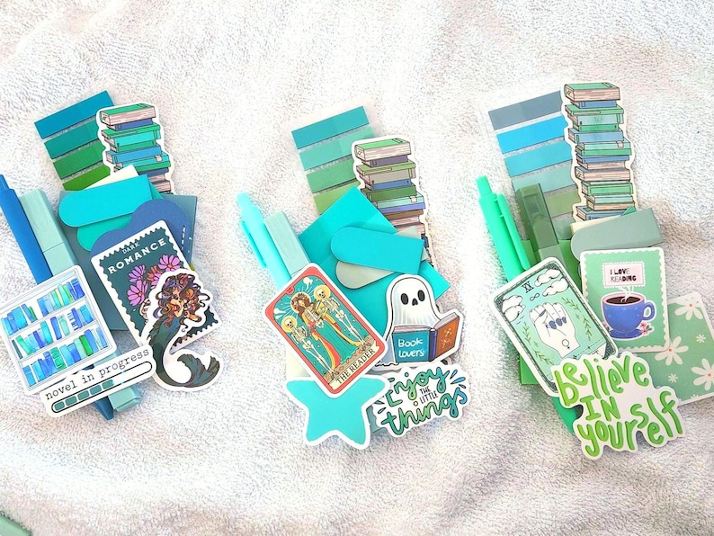 Peut inclure: Trois ensembles de fournitures de papeterie dans des tons bleu et vert, comprenant divers autocollants dont une pile de livres, une sir&egrave;ne, un fant&ocirc;me lisant, des cartes de tarot et les textes "Novel in progress", "Enjoy the little things" et "Believe in yourself."
