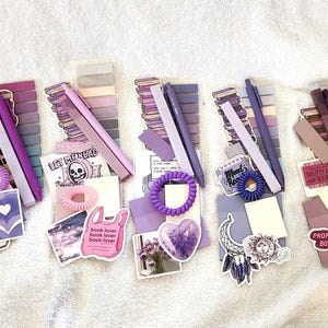 Peut inclure: Cinq ensembles de papeterie dans des tons violets, chacun comprenant une pile de notes adh&eacute;sives, un stylo, un &eacute;lastique &agrave; cheveux en spirale et divers autocollants avec du texte comme Chasing that Scholastic, Let Me Read et Professional Book Worm.